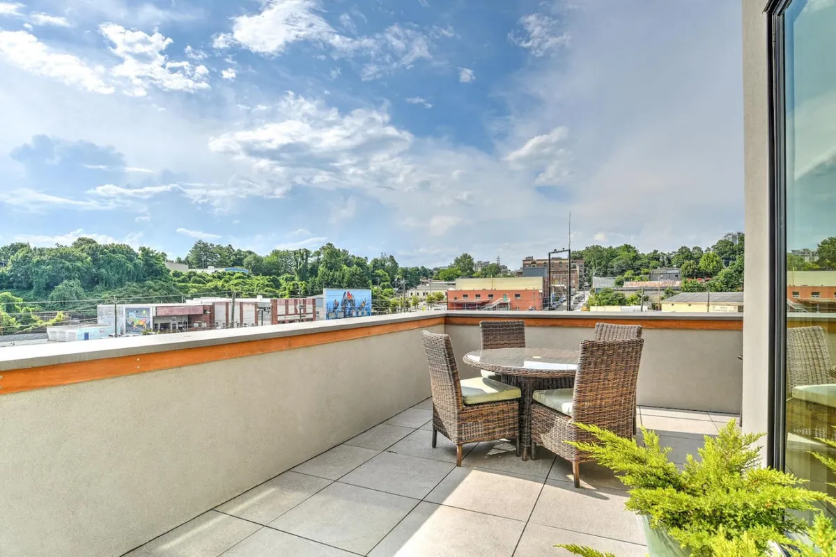 A cozy outdoor seating arrangement occupies a rooftop or terrace space with clear views of the city skyline. A potted plant adds a touch of nature, while the layout invites both intimate morning coffee moments and evening gatherings. The relaxed atmosphere is perfect for enjoying sunsets or tranquil downtime above the city.
