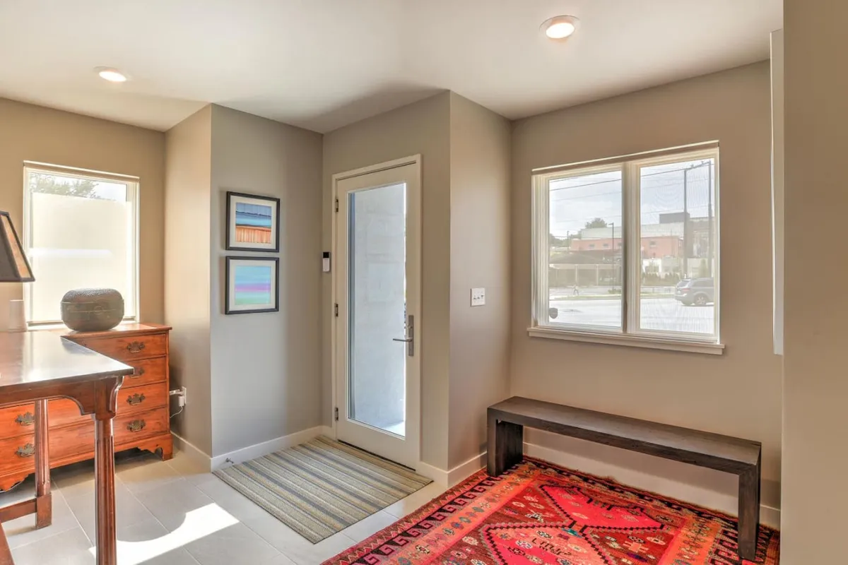 This image captures a welcoming entry foyer featuring a wooden dresser, colorful artwork, and a striped rug alongside a bench. The setup suggests a space ideal for first impressions, greeting guests, and transitioning into the home.