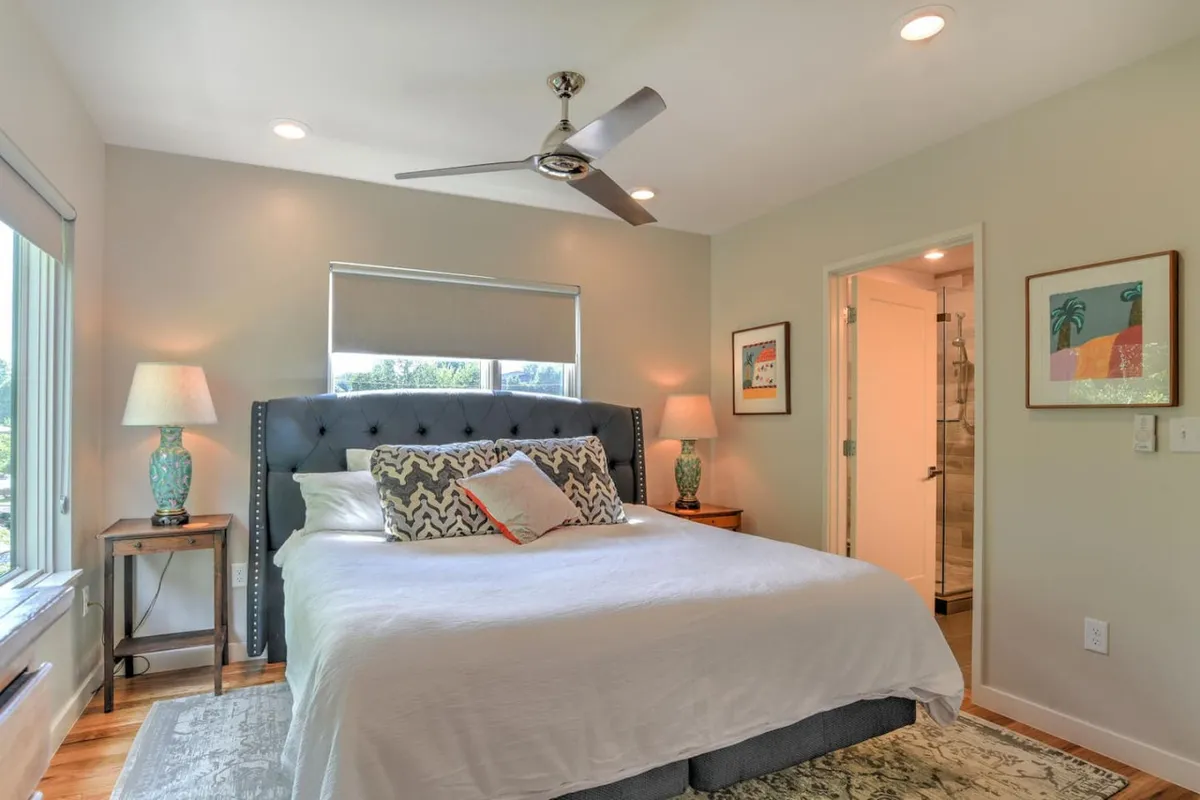 A tranquil primary bedroom featuring a king-sized bed dressed in soft linens, with decorative pillows and matching table lamps on each side. Natural light streams through a window offering a soothing view, while the neutral color palette and uncluttered decor create a peaceful, private atmosphere ideal for rest and retreat.