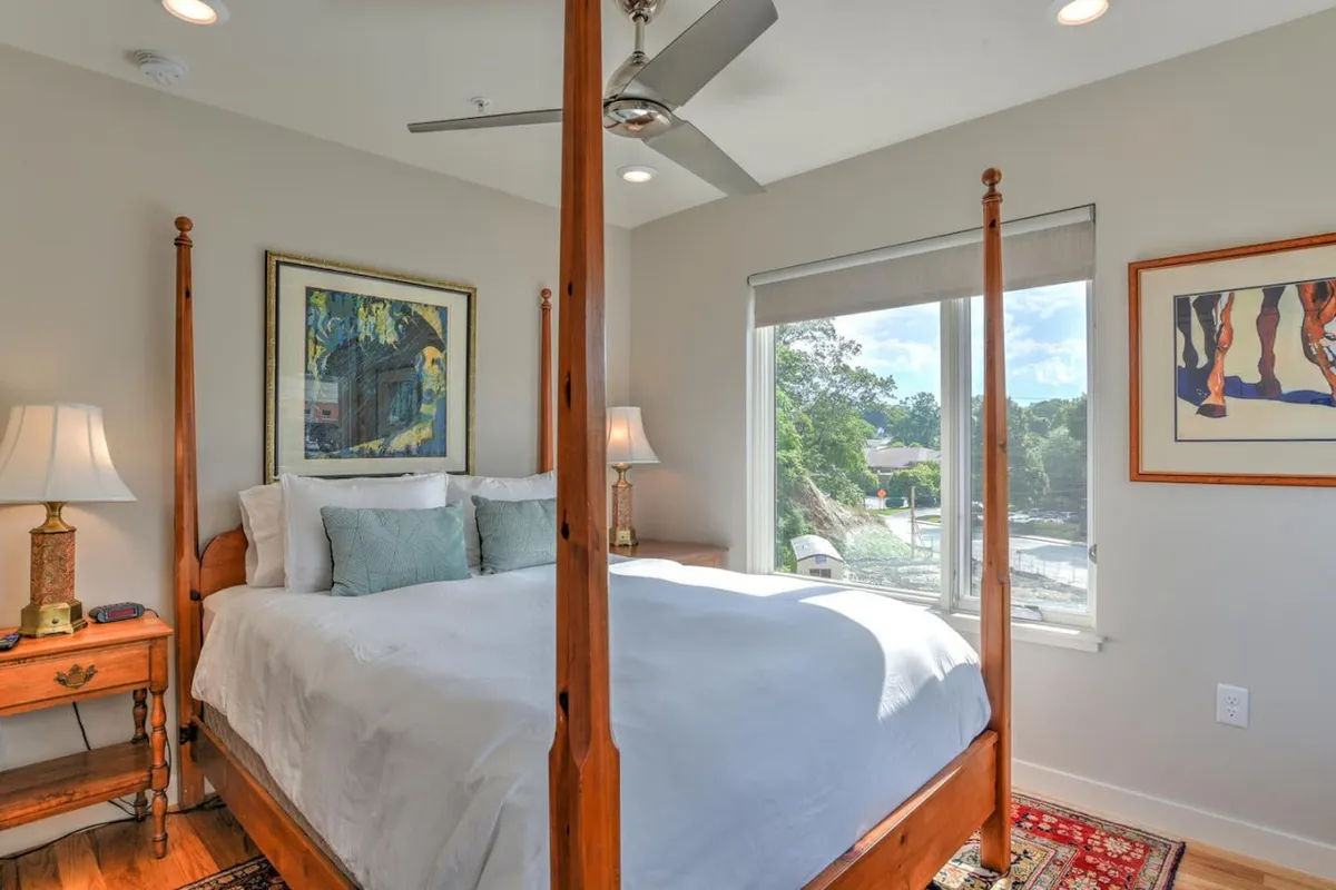 A spacious queen bedroom with a classic four-poster bed, elegant artwork, bedside lamps, and a window overlooking the outdoors. The room is styled for comfort and relaxation, providing a welcoming space for guests or children.