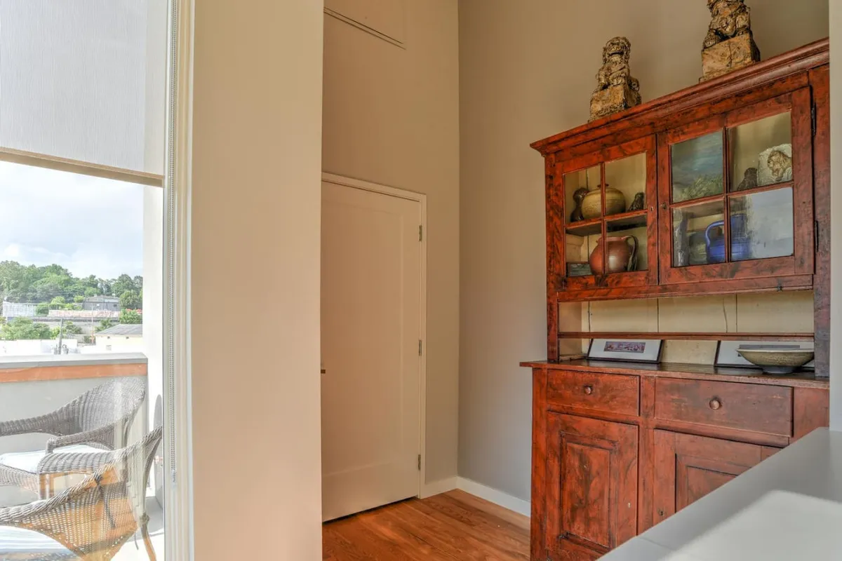 This image focuses on an antique cabinet adorned with decorative items, with a window offering a view to the outside. The scene conveys a connection between interior comfort and the outdoors, suggesting the possibility of enjoying scenic vistas from within the property.